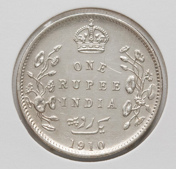 Das Bild zeigt die Rückseite (Revers) mit dem Nennwert ONE RUPEE INDIA und der Jahreszahl 1910, gekrönt von der britischen Krone und umgeben von einem detailreichen floralen Kranz. Die Münze zeigt eine attraktive, authentische Patina