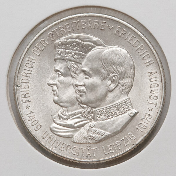Nahaufnahme der Gedenkmünze von 1909 zum Universitätsjubiläum Leipzig. Zu sehen ist das Doppelbildnis von Friedrich dem Streitbaren und König Friedrich August III. im Profil. Die Umschrift lautet 1409 UNIVERSITÄT LEIPZIG 1909. Die Details der Porträts sind gestochen scharf.