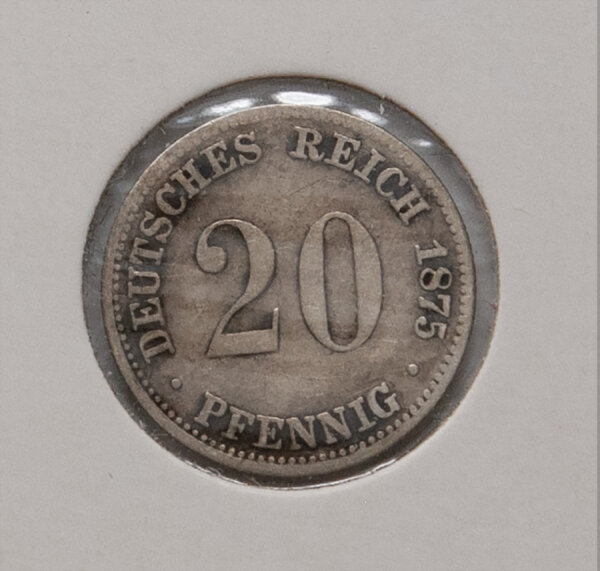 Nahaufnahme der Wertseite der 20-Pfennig-Silbermünze von 1875. Zentral ist die große 20 zu sehen, darunter der Schriftzug PFENNIG. Die Umschrift lautet DEUTSCHES REICH 1875. Die Münze zeigt eine dunkle Alterspatina.